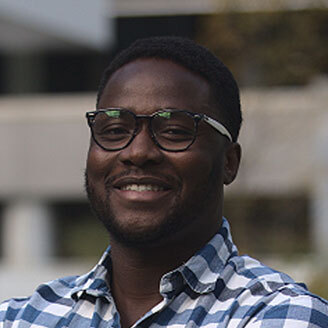 University student with a bright smile, sporting glasses and a checkered shirt, exudes confidence and approachability.