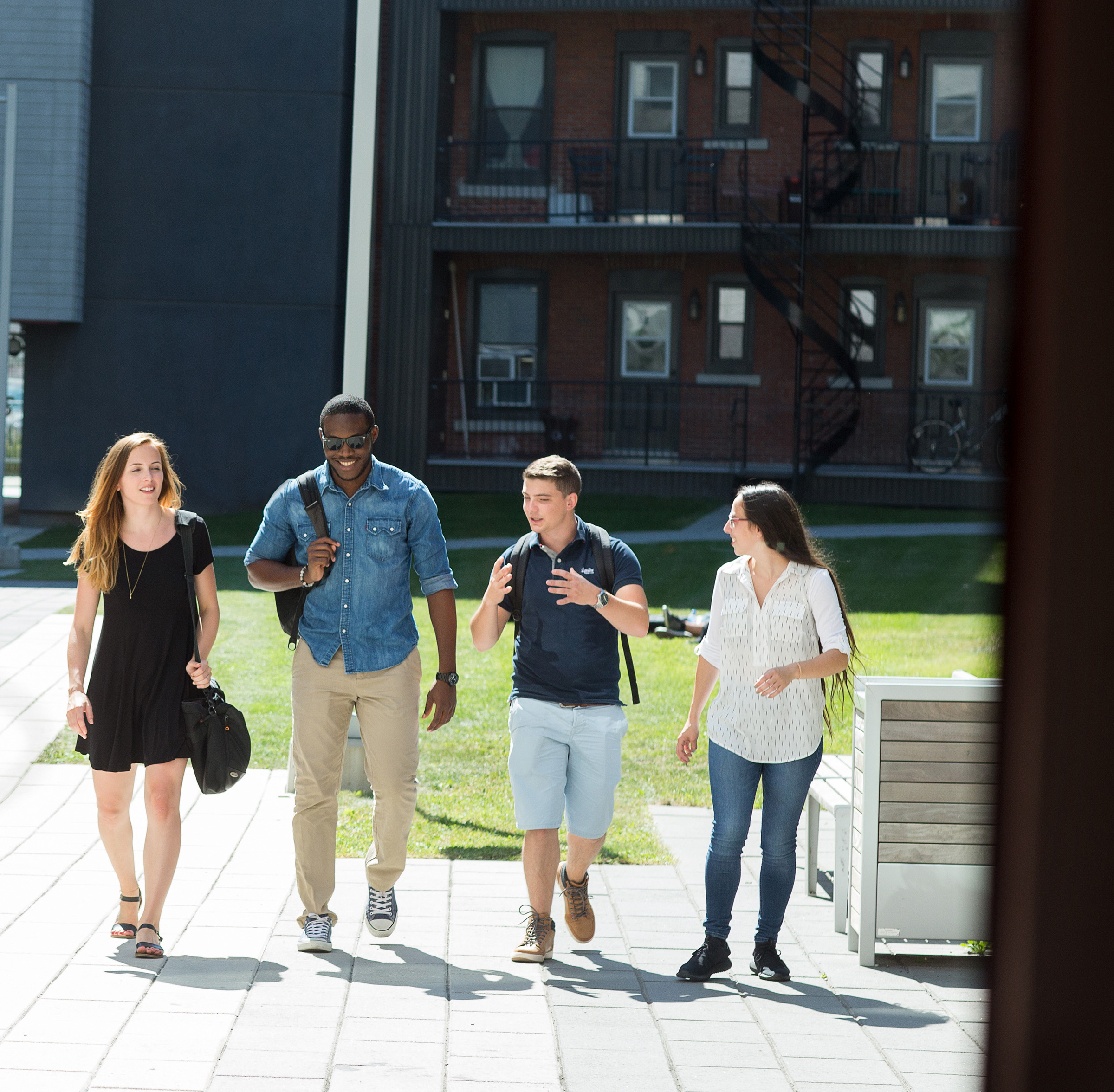 Étudiants souriants se promenant sur le campus universitaire par beau temps.