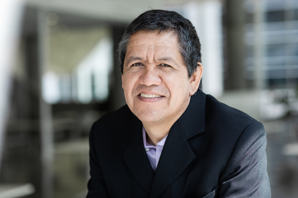 Esteemed professor smiling, office building backdrop, showcasing expertise and leadership.