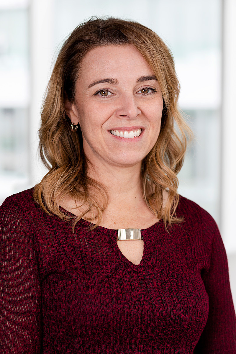 Professional female staff member with a friendly smile, wearing a maroon sweater and a necklace.