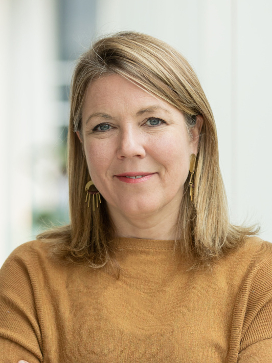 Faculty member in tech with a warm smile, standing indoors, embodying experience and approachability.