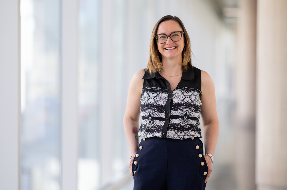 Professionnelle souriante en tenue de travail, posant dans un couloir lumineux.