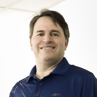 Professeur souriant en polo bleu, fond clair, évoquant professionnalisme et accessibilité.