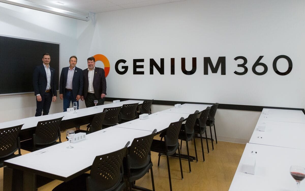Three professionals stand in a modern meeting room with the logo "GENIUM 360" displayed prominently.