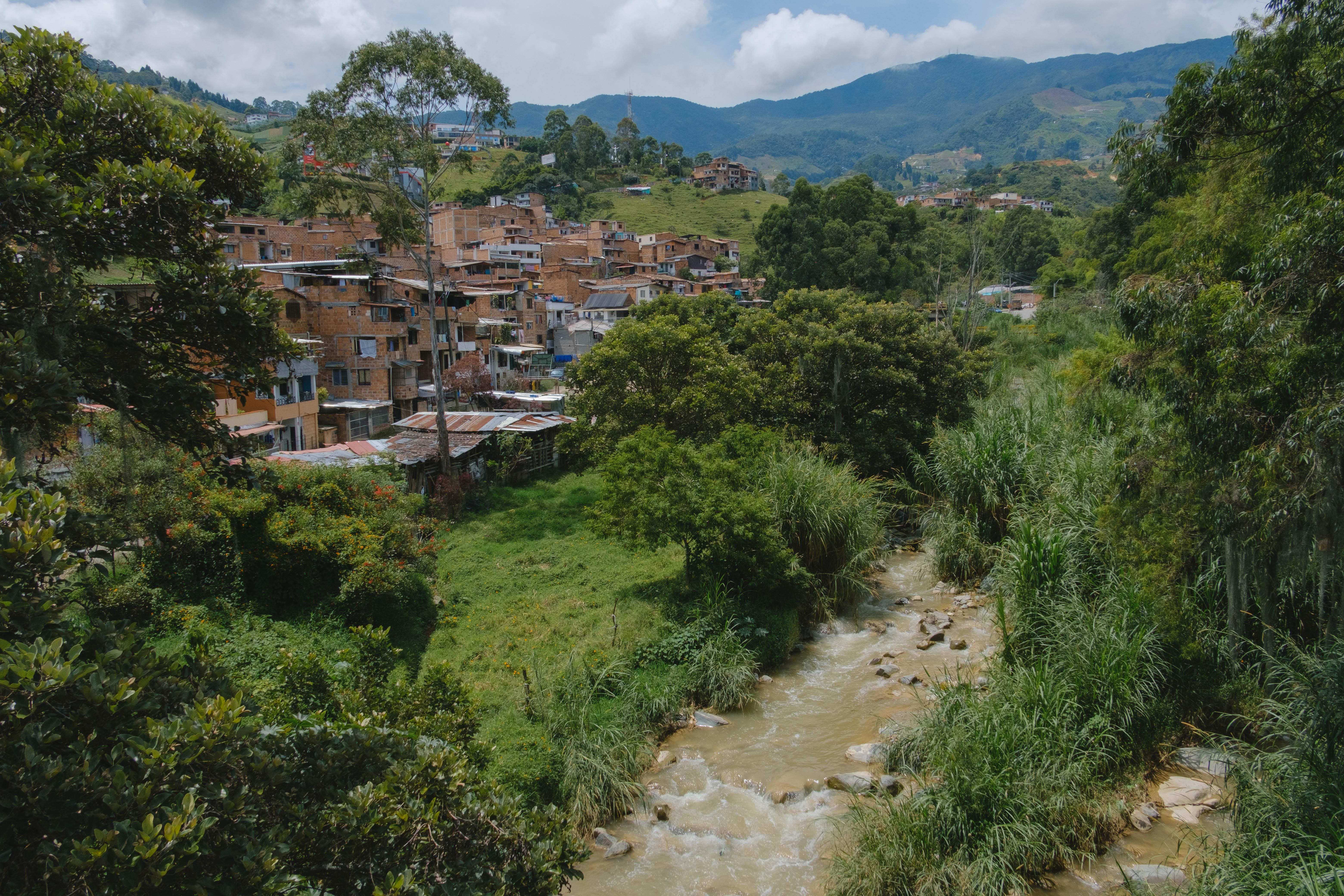 Vue panoramique d'un quartier dense entouré de verdure, avec un ruisseau serpentant à travers un paysage montagneux.