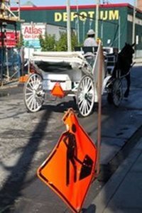 Une calèche, menée par un caléchier que l'on aperçoit de dos, se trouve sur une rue de Griffintown et se déplace sur une rue où est installé un chantier de construction dans le quartier Griffintown.