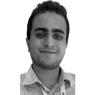 Staff member: young male, short dark hair, beard, smiling, wearing a light shirt; embodies professionalism.