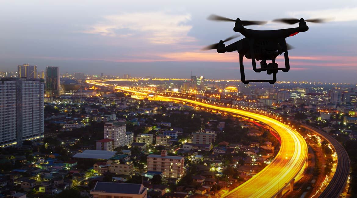 Vue de drone au crépuscule, ville lumineuse et routes sinueuses.