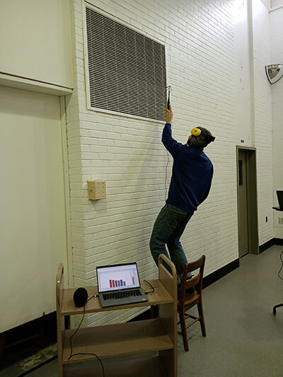 Un étudiant effectue des mesures à l'aide d'un équipement, en utilisant une échelle pour atteindre un espace en hauteur.
