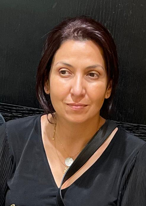 Une femme souriante aux cheveux bruns, vêtue de noir, dégage une impression de sérénité et de confiance dans son regard.