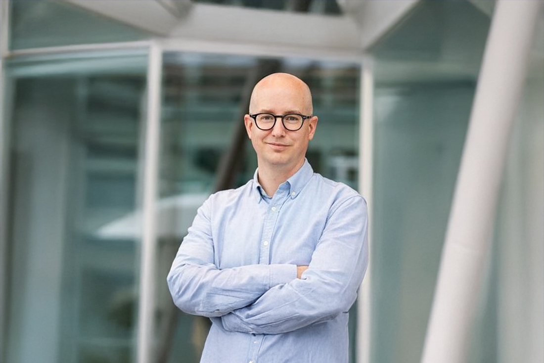 Un homme souriant, prêt à inspirer et à partager son expertise en technologie supérieure. Contexte professionnel.