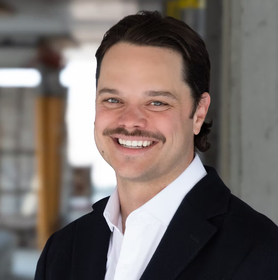 Un professionnel souriant en costume, prêt à inspirer et à partager son expertise en technologie supérieure. Contexte moderne et dynamique.