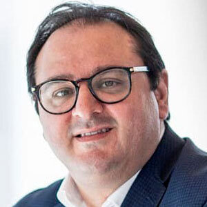 Portrait d'un professionnel souriant, portant des lunettes et un costume, symbolisant l'innovation et l'expertise en technologie.