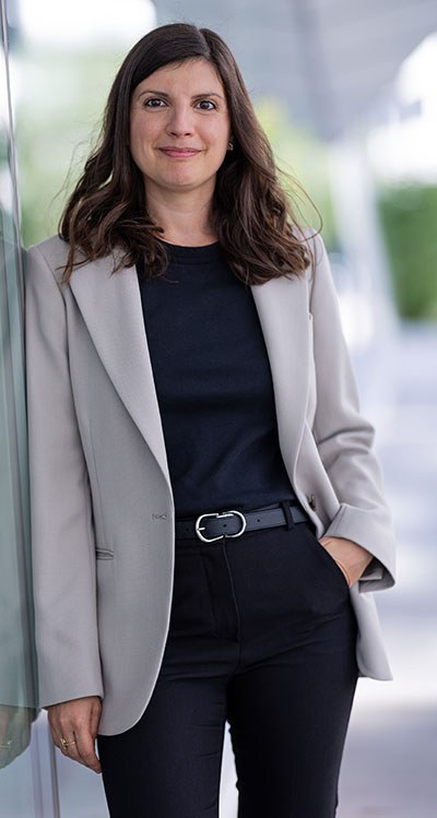 A professional individual confidently poses in a stylish blazer and black attire, set against a modern backdrop.