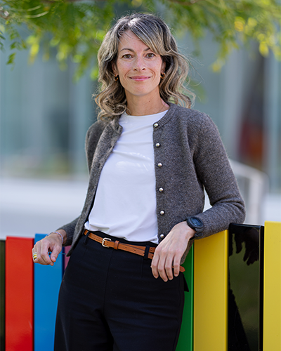 Un portrait d'une femme souriante, élégamment vêtue, posant avec confiance devant des couleurs vibrantes. Atmosphère accueillante et dynamique.
