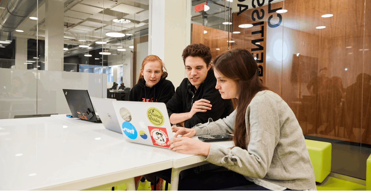 Students collaborate around a laptop in a modern, bright workspace, exchanging ideas and solutions.