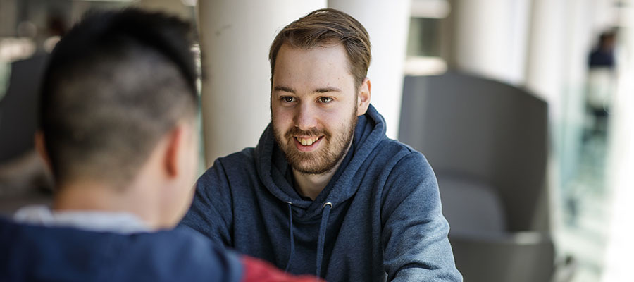 Deux étudiants échangent dans un espace moderne, illustrant la convivialité et l'interaction au sein de l'université.
