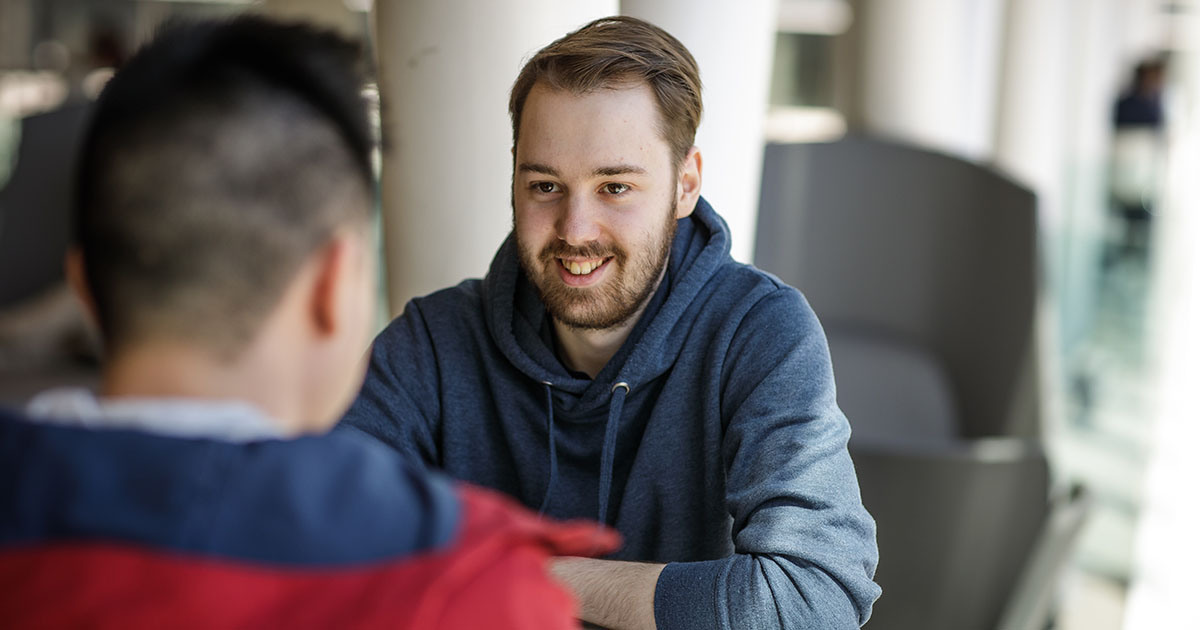 Deux étudiants échangent dans un environnement convivial et moderne, favorisant la collaboration et l'apprentissage.