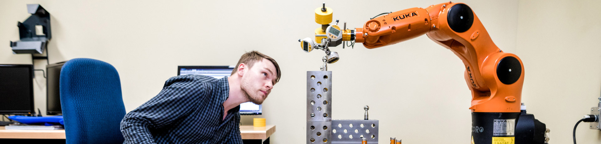 Étudiant interagissant avec un bras robotique KUKA en laboratoire.