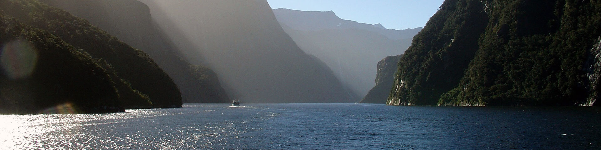 Fjord majestueux avec rayons solaires, falaises abruptes et bateau naviguant.