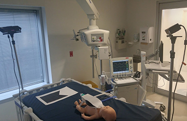 Salle de simulation médicale équipée d'un mannequin, d'un moniteur et de divers instruments.