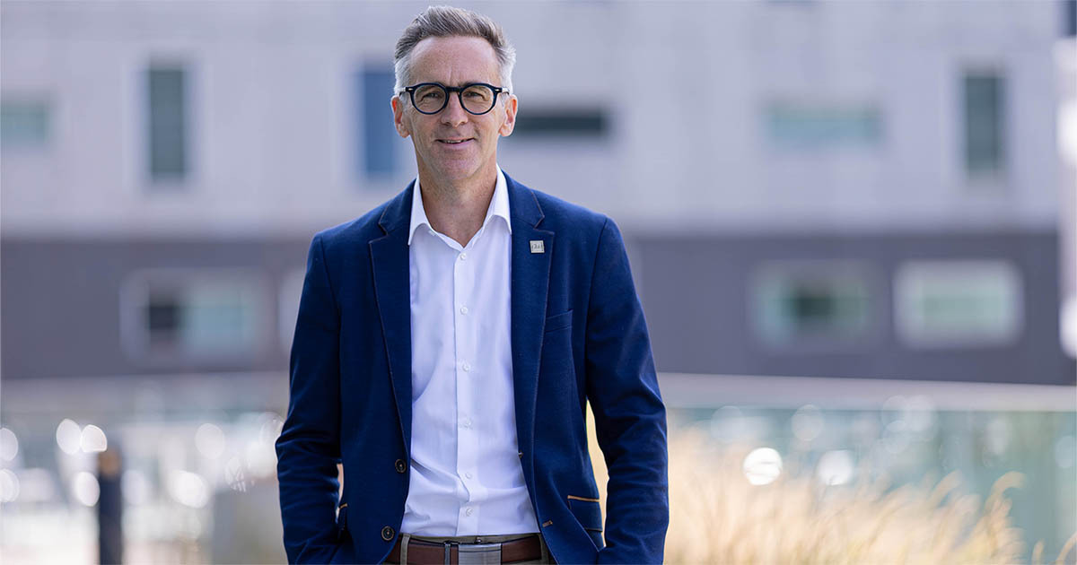 A smiling man in a blue blazer stands confidently in a modern setting, exuding confidence and professionalism.