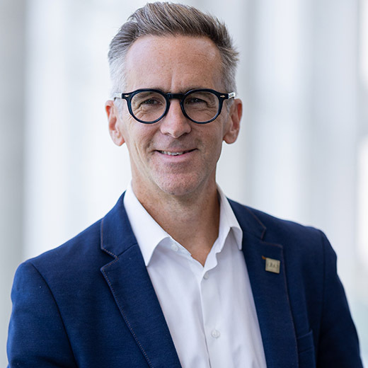 Un professionnel souriant en tenue décontractée, affichant un style moderne, se tient devant un fond lumineux.