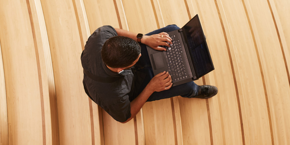 Un étudiant travaille sur son ordinateur portable, installé confortablement sur des bancs en bois dans un cadre moderne et inspirant.