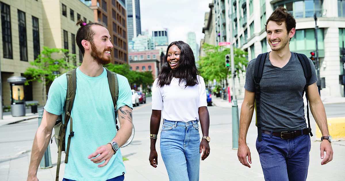 Trois étudiants souriants se promènent dans un cadre urbain.