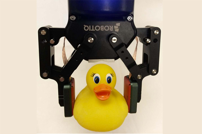 Bras robotique tenant un canard jaune, démontrant la précision et la délicatesse de la technologie.