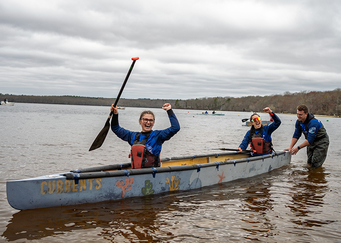 Des étudiants s'amusent en canoë sur un lac, célébrant une réussite collective sous un ciel nuageux.