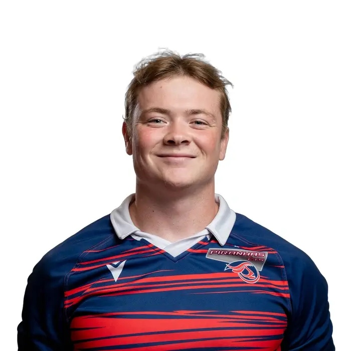 Jeune homme souriant portant un maillot de rugby bleu et rouge, affichant une attitude confiante et amicale.