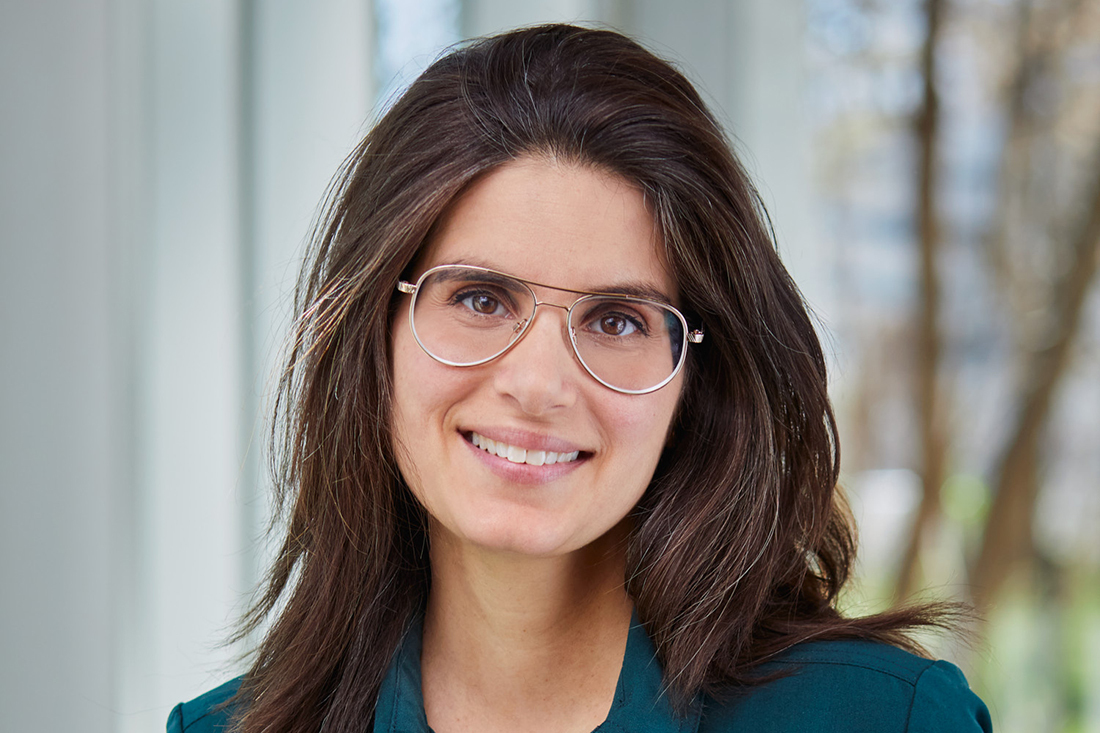 Professeure souriante en technologie avec lunettes et blouse verte.