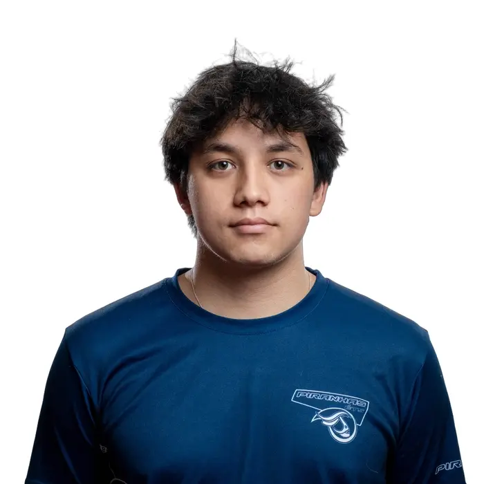 Un étudiant en technologie porte un t-shirt rouge avec le logo de l'équipe Piranhas, affichant un regard sérieux et déterminé.
