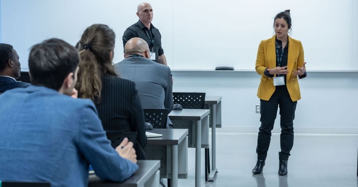 Une intervenante présente un sujet devant un public attentif lors d'une session académique. Ambiance de partage et d'échange.