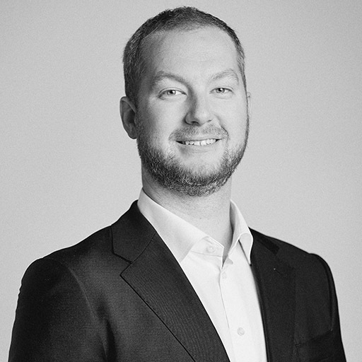 Un homme souriant en costume, portant une chemise blanche, dégage une impression de professionnalisme et de confiance.