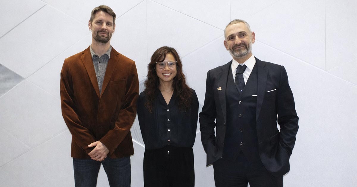 Three professionals dressed in formal attire, standing together against a modern backdrop, showcasing a collaborative atmosphere.