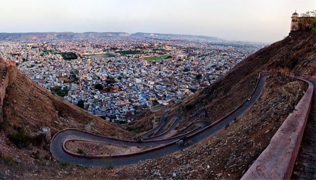 Vue panoramique d'une ville dense depuis une route sinueuse en montagne.
