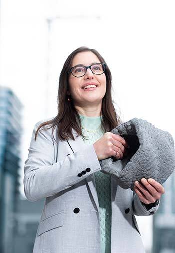 Femme en tenue professionnelle souriante, empreinte de confiance, évoquant l'innovation et le progrès.