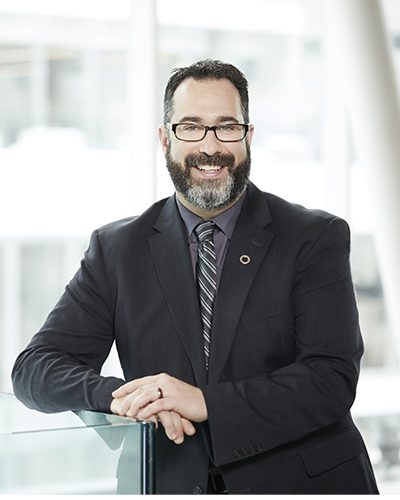 Un professionnel souriant en costume, posant avec confiance, dans un cadre moderne et lumineux. Ambiance accueillante et dynamique.