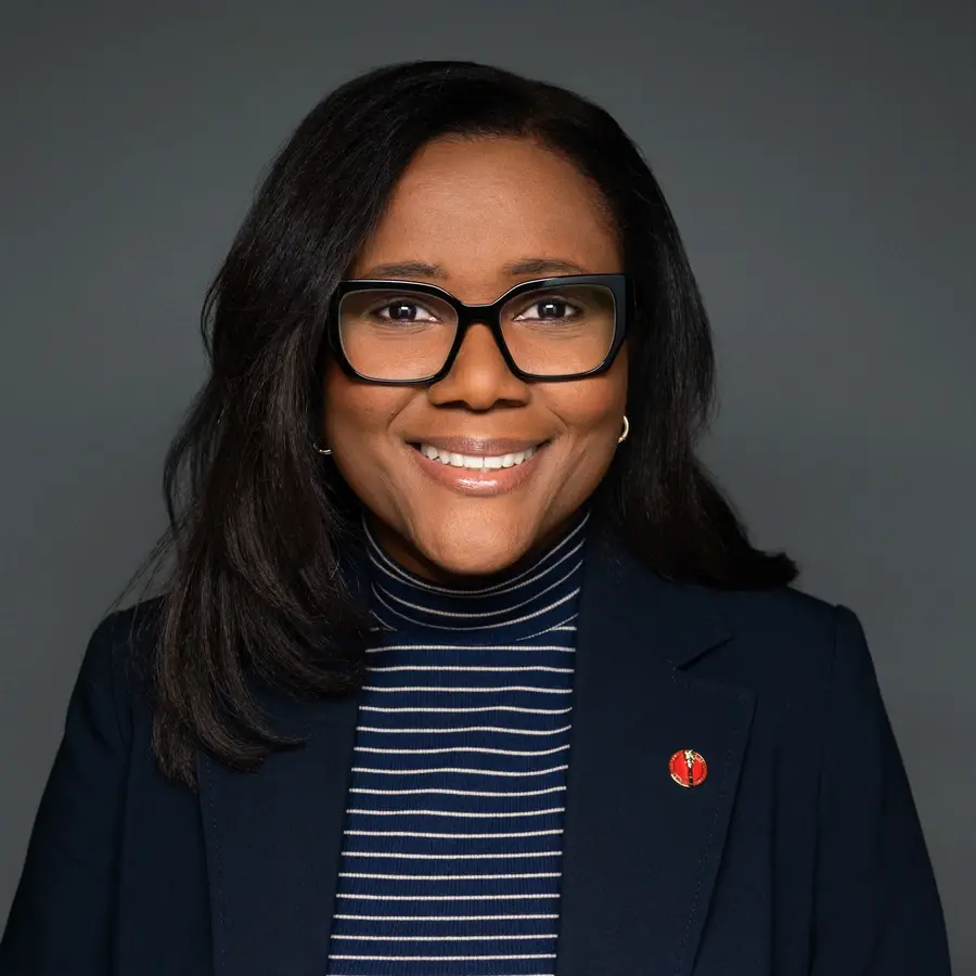 Portrait d'une professionnelle souriante, portant des lunettes et un vêtement sombre, avec une ambiance conviviale et chaleureuse.