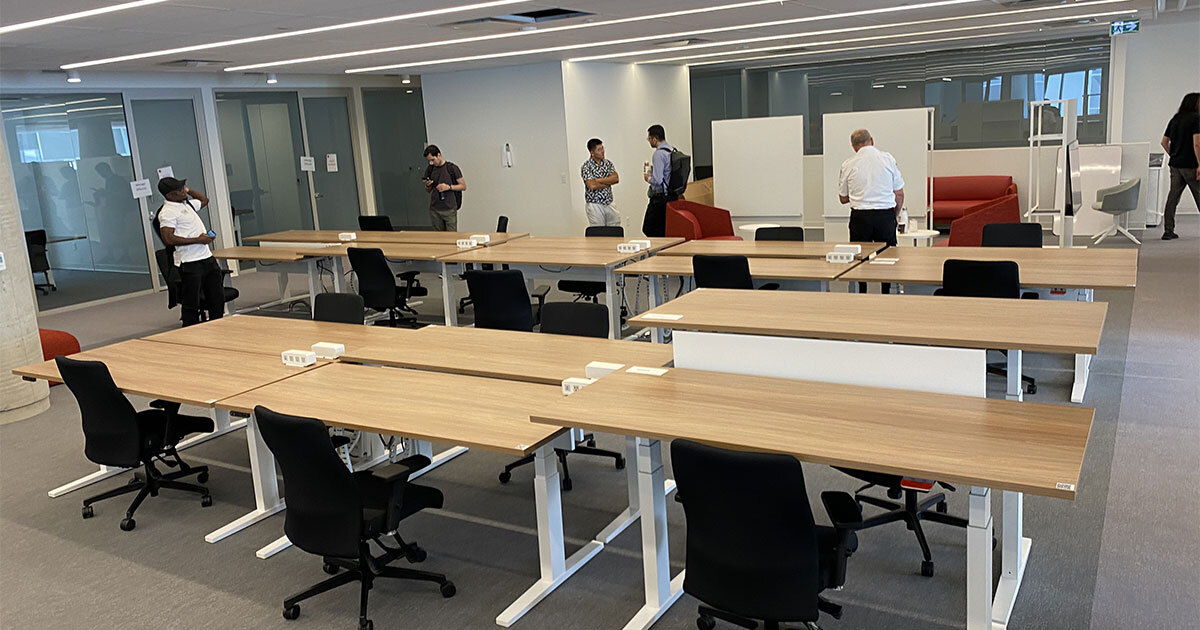Salle moderne avec des bureaux et chaises, des gens debout discutent.