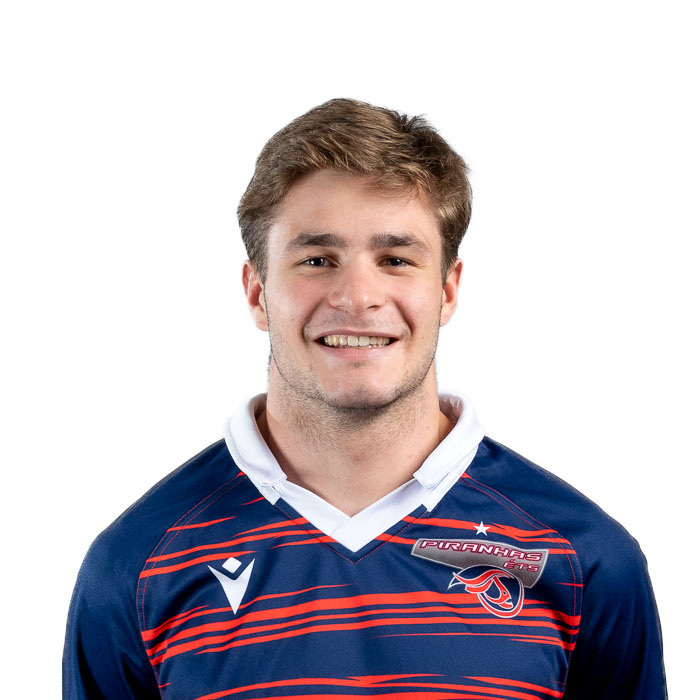 Joueur de rugby souriant, portant un maillot aux couleurs des Piranhas. Ambiance sportive et dynamique.