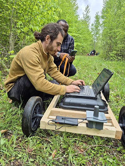 Des étudiants travaillent sur un projet technologique en plein air, utilisant un ordinateur portable monté sur un chariot.