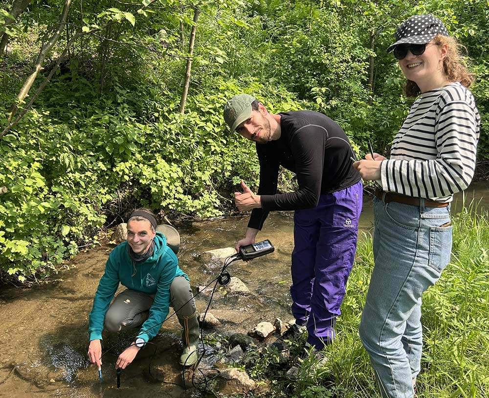 Des étudiants effectuent des recherches sur le terrain, examinant l'eau d'un cours d'eau tout en prenant des notes.