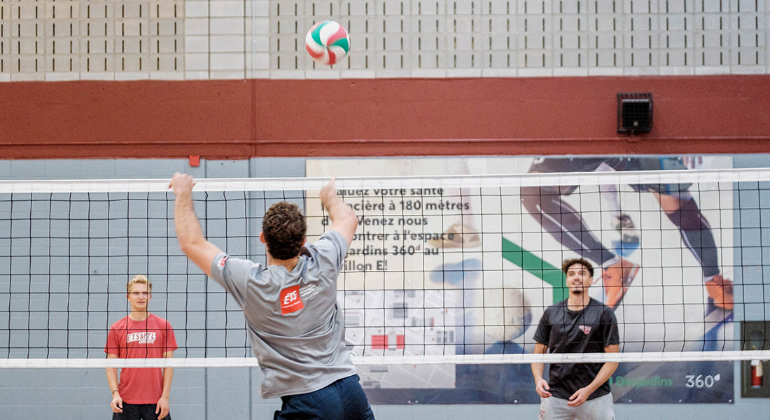 Des étudiants s'entraînent au volleyball, concentrés sur le jeu, dans une ambiance sportive et dynamique.