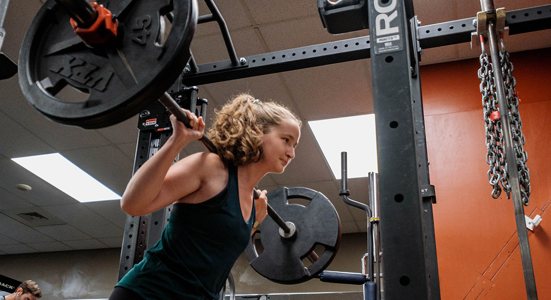 Une athlète s'entraîne avec des poids dans une salle de sport moderne, mettant en avant sa concentration et son effort.