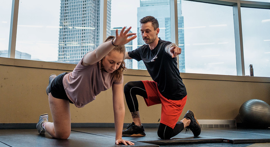 Un entraîneur guide une jeune élève dans un exercice de fitness, favorisant le développement physique dans un espace moderne et lumineux.