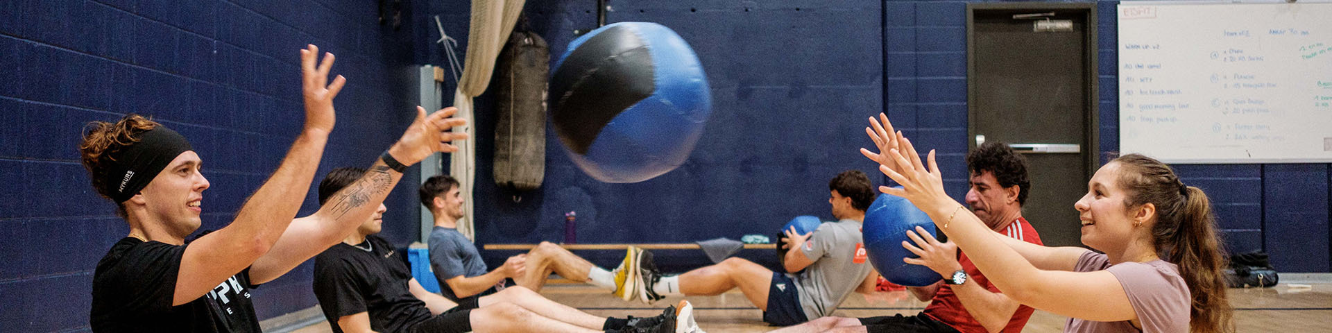 Des étudiants s'entraînent ensemble dans un gymnase, échangeant une balle médicinale pour renforcer leur forme physique et leur cohésion d’équipe.
