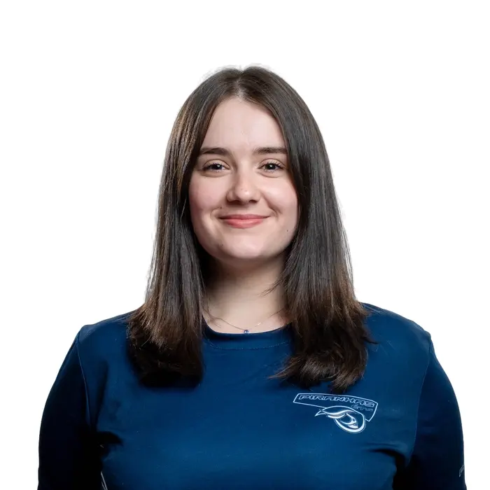 Étudiante souriante en chandail bleu, a les cheveux bruns lousses. Représente le dynamisme universitaire.